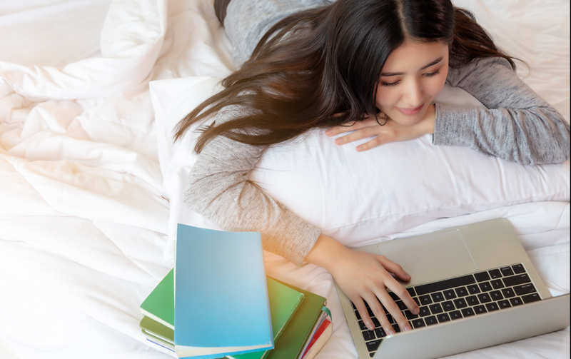 College student doing homework on dorm bed